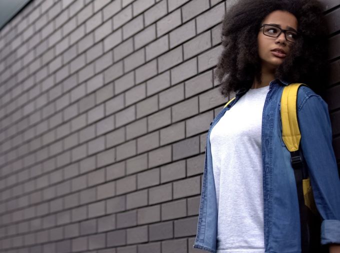 Student along a brick wall, looking afraid, unsure.